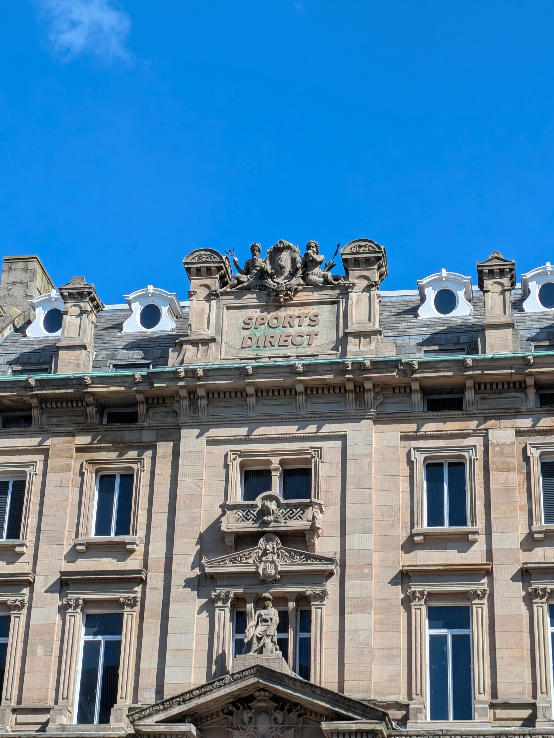 A historic building facade features ornate architectural details and a Sports Direct sign.