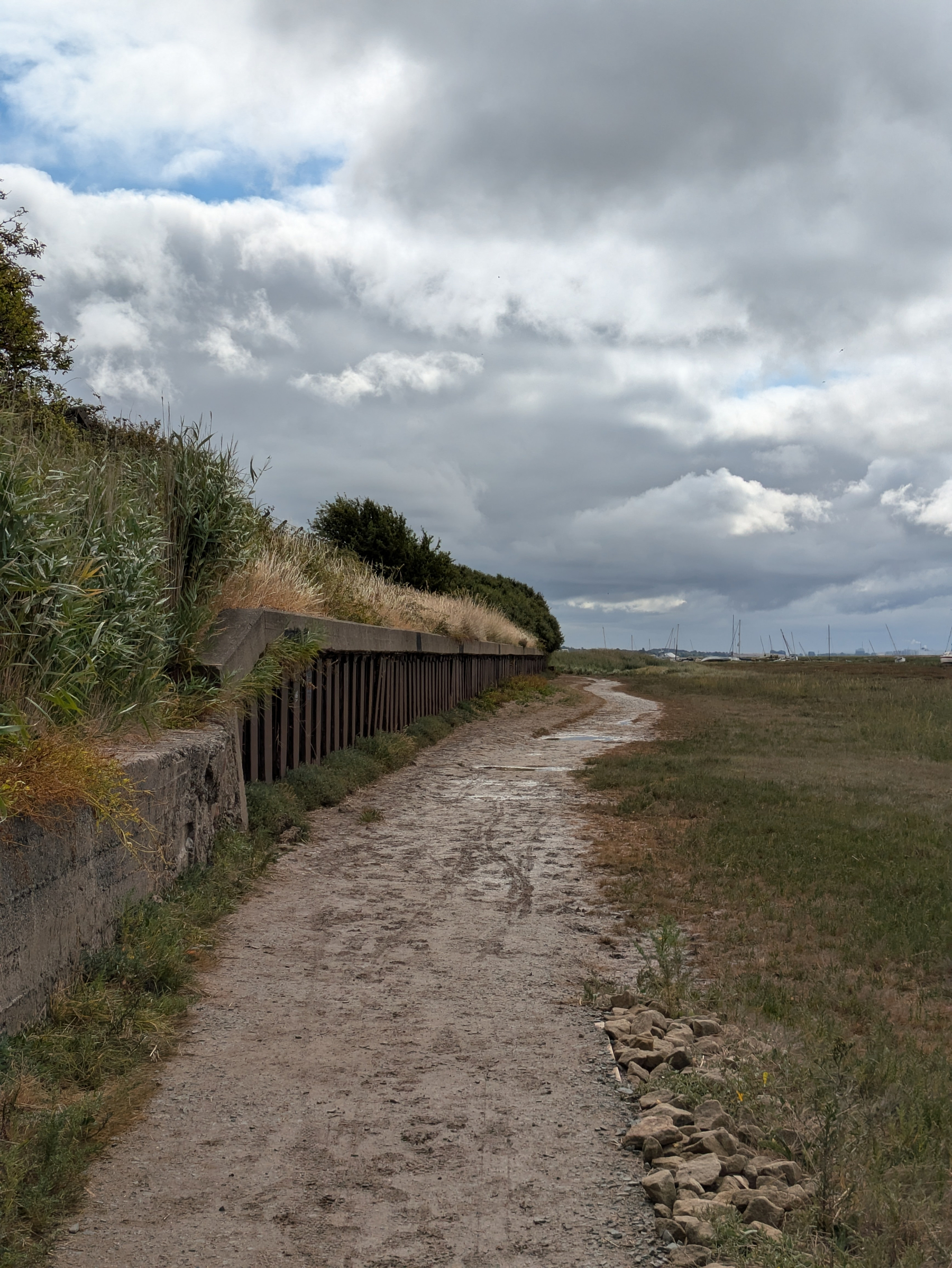 A winding dirt path runs alongside a grassy embankment beneath a cloudy sky.