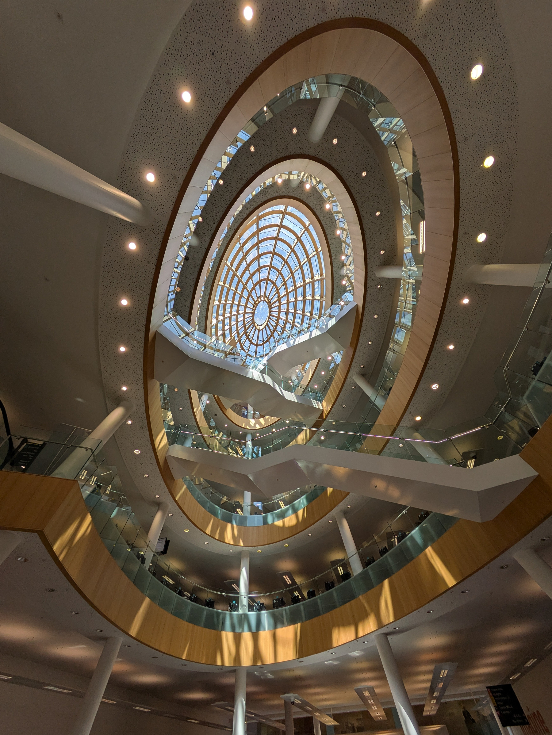 Looking up through a multi-story atrium with circular balconies, the view showcases a large, intricate dome skylight.