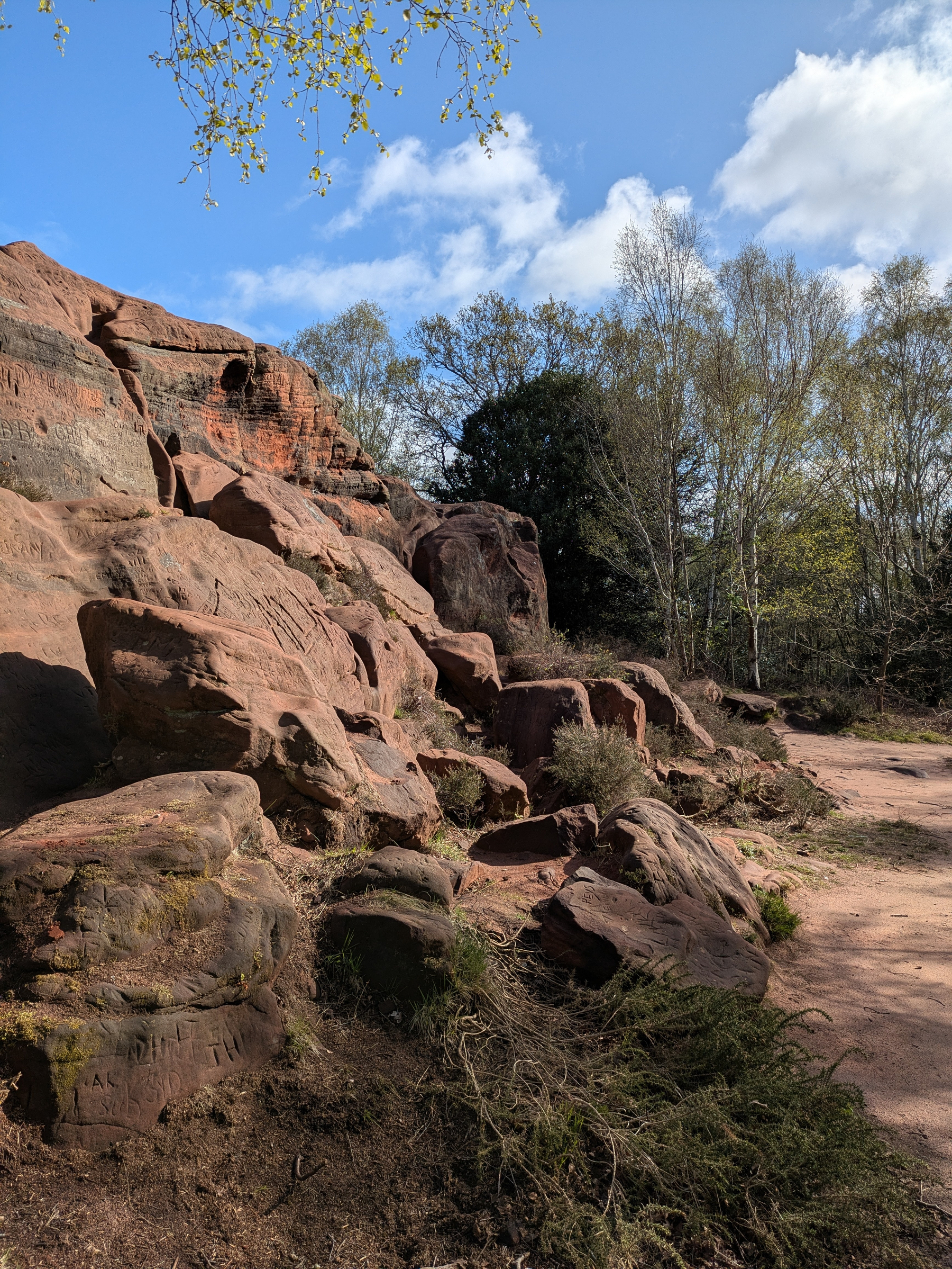 Red sandstone rocks are surrounded by trees under a partly cloudy sky.