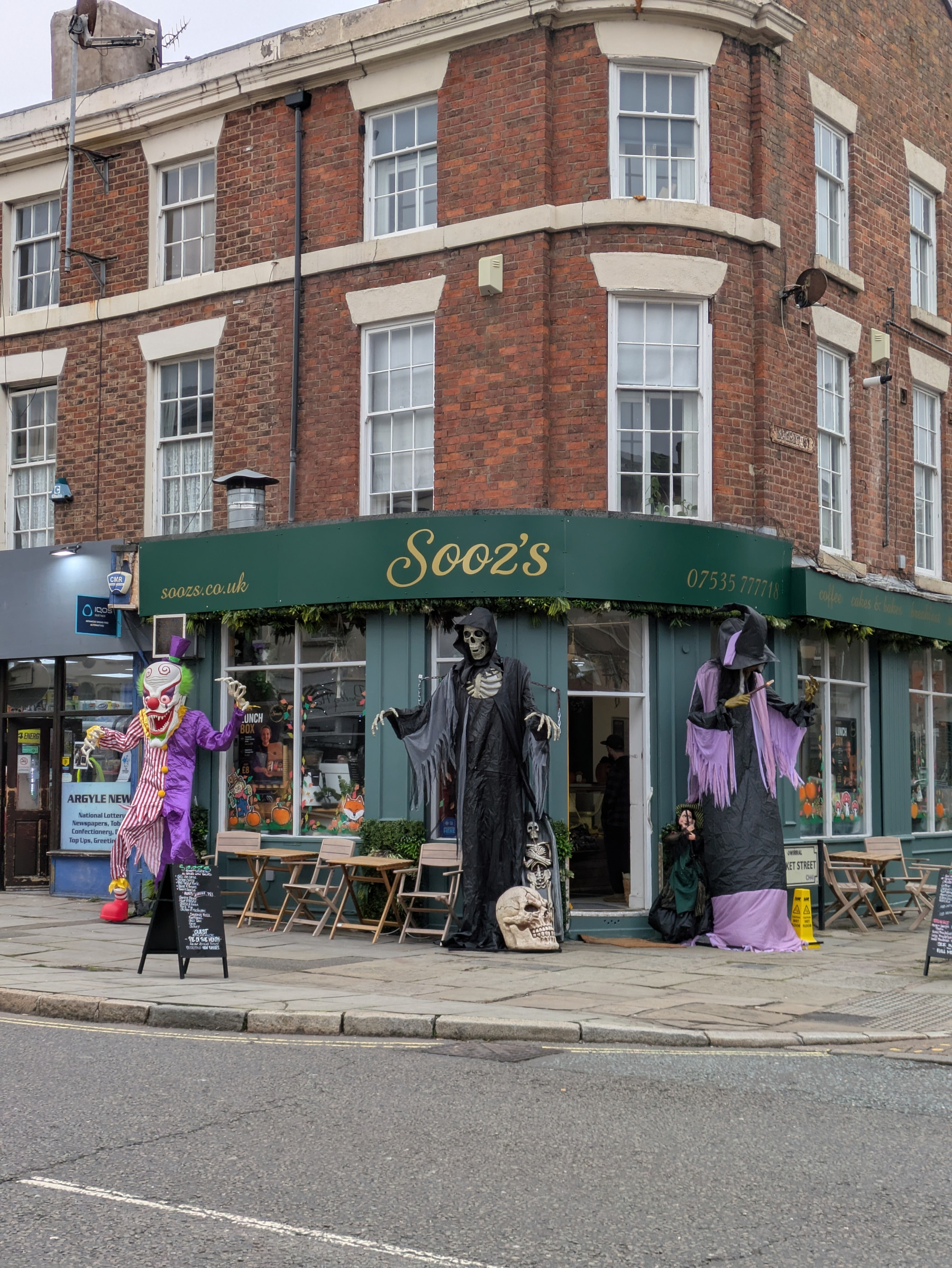 A corner shop named Sooz’s is decorated with large Halloween figures, including a clown, a grim reaper, and a witch.
