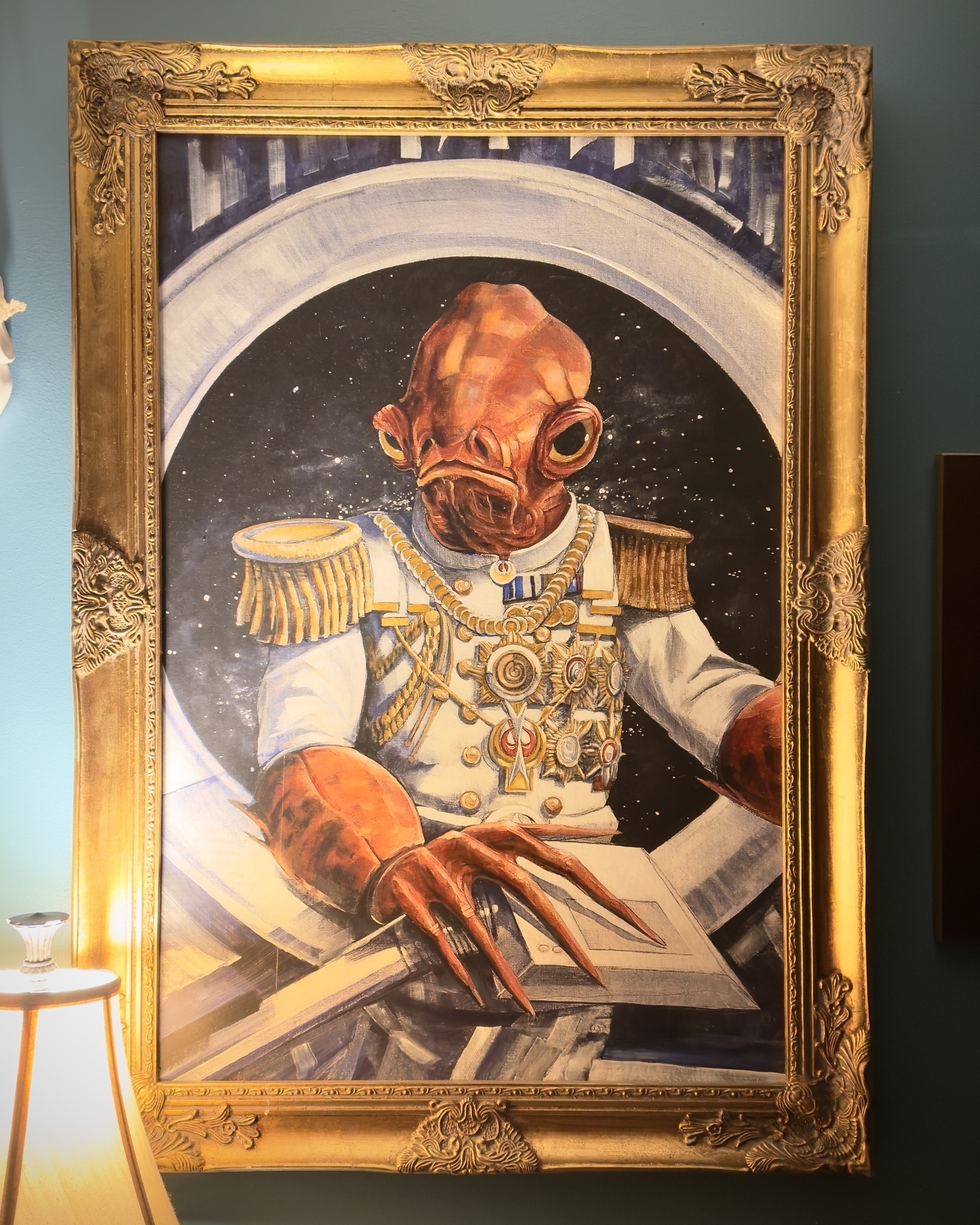 A painting of Admiral Ackbar in formal dress, in a fancy gilded frame, on the wall of the bathroom in River City Tattoo.