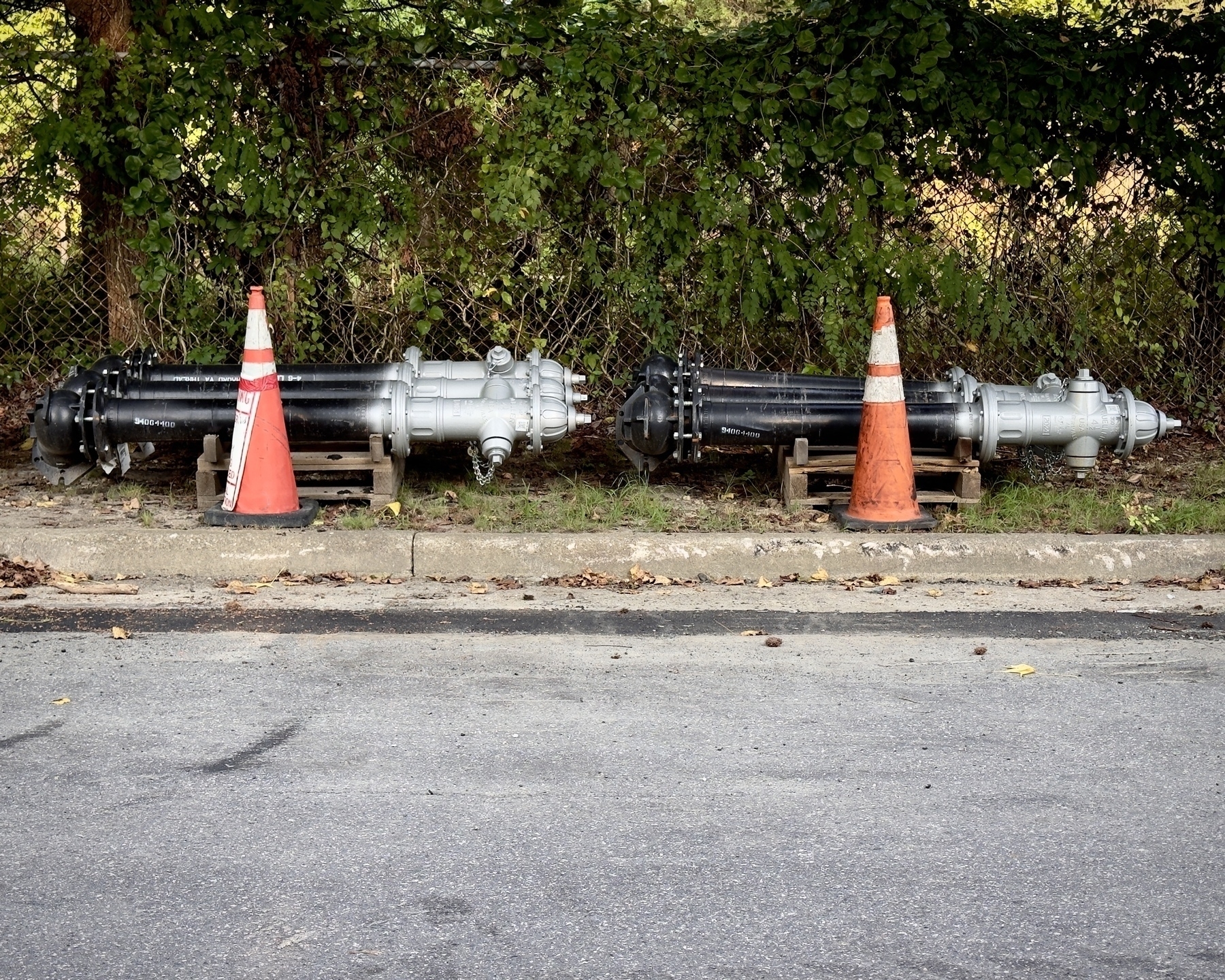 Two stacks of fire hydrants with connecting pipes, each stack behind a traffic cone, on the side of a road