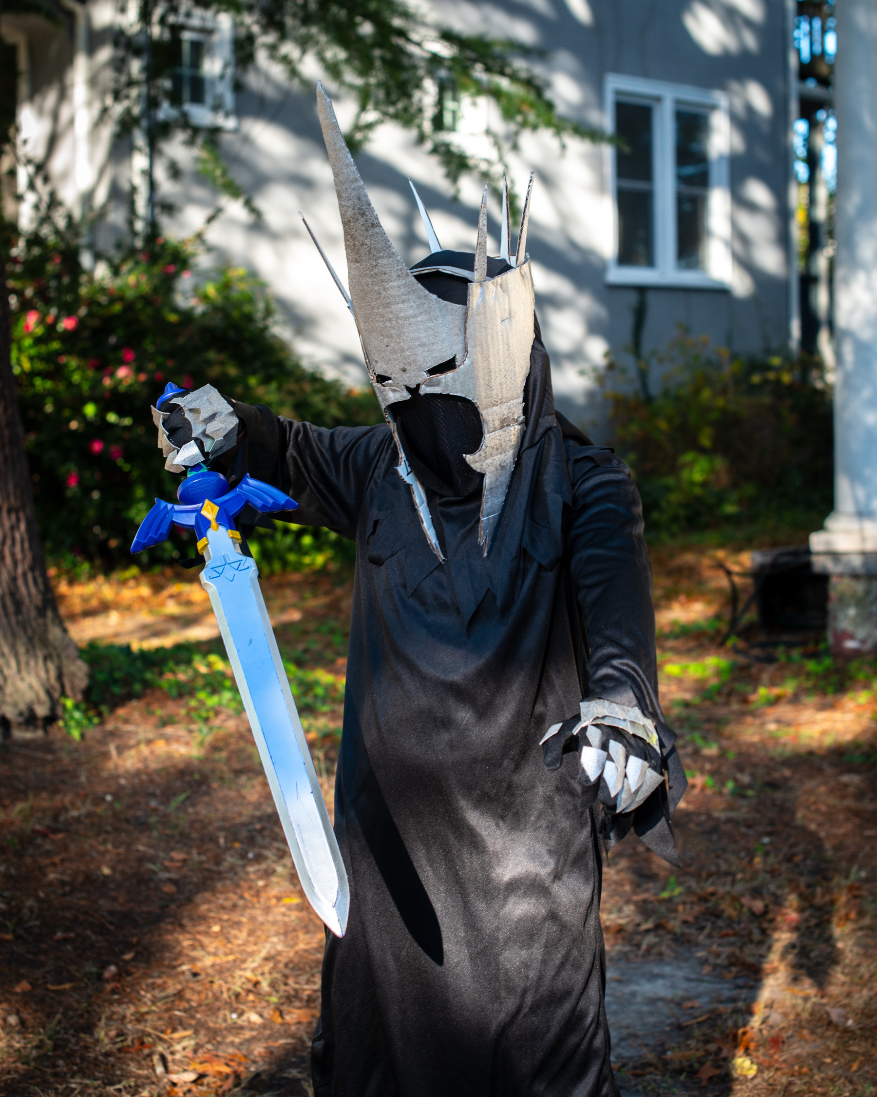 my son wearing a costume of all black with a silver cardboard crown and silver cardboard gloves, holding a plastic Master Sword from The Legend of Zelda games