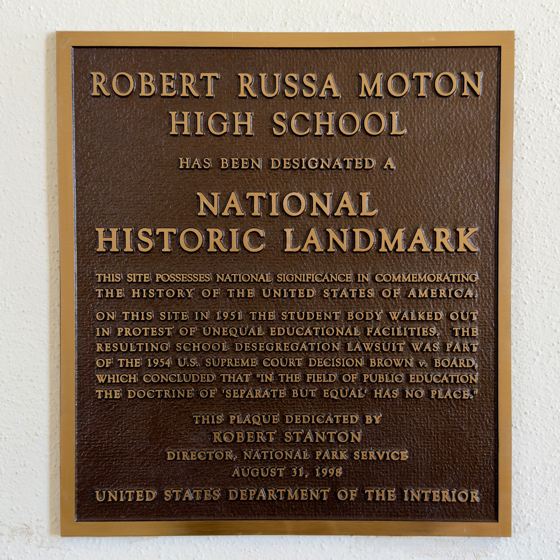 Historic marker plaque in the Moton Museum reading: “ROBERT RUSSA MOTON&10;HIGH SCHOOL&10;HAS BEEN DESIGNATED A NATIONAL&10;HISTORIC LANDMARK&10;THIS SITE POSSESSES NATIONAL SIGNIFICANCE IN COMMEMORATING THE HISTORY OF THE UNITED STATES OF AMERICA,&10;ON THIS SITE IN 1951 THE STUDENT BODY WALKED OUT IN PROTEST OF UNEQUAL EDUCATIONAL FACILITIES. THE RESULTING SCHOOL DESEGREGATION LAWSUIT WAS PART OF THE 1954 U.S. SUPREME COURT DECISION BROWN. BOARD, WHICH CONCLUDED THAT IN THE FIELD OF PUBLIC EDUCATION THE DOCTRINE OF 'SEPARATE BUT EQUAL HAS NO PLACE."&10;THIS PLAQUE DEDICATED BY&10;ROBERT STANTON&10;DIRECTOR, NATIONAL PARK SERVICE&10;AUGUST 31, 1998&10;UNITED STATES DEPARTMENT OF THE INTERIOR”