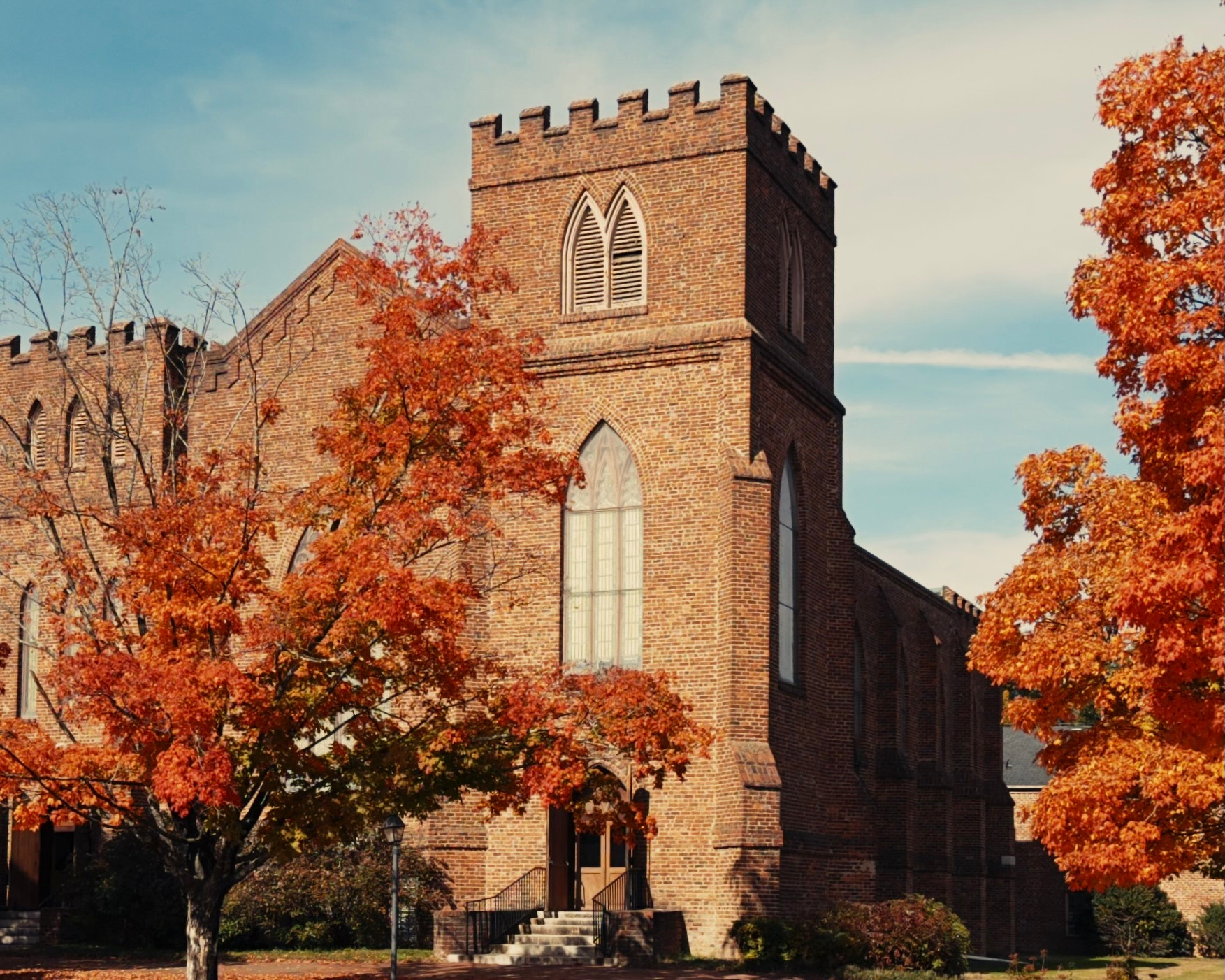 A church bus behind some trees with orange leaves
