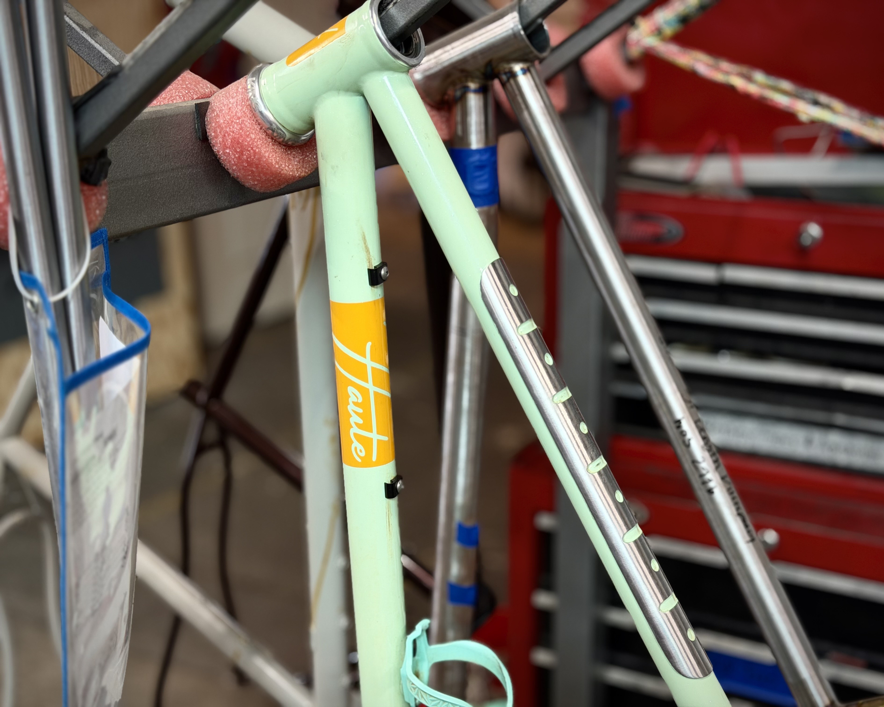 close-up of a Haute bike with a polished top tube decoration over an otherwise mint green paint job and orange block around a Haute logo