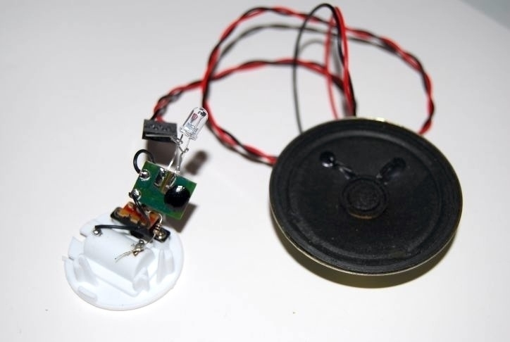 An LED tea light which has been cracked open so wires can be connected from its chip to a speaker. 