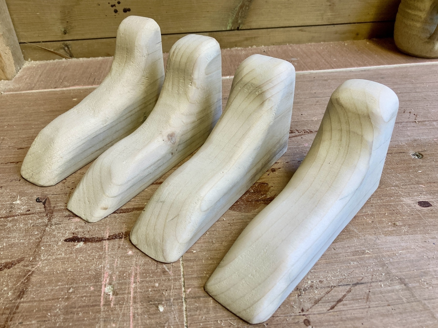 Four wooden shelf brackets on a workbench, all sanded smooth.