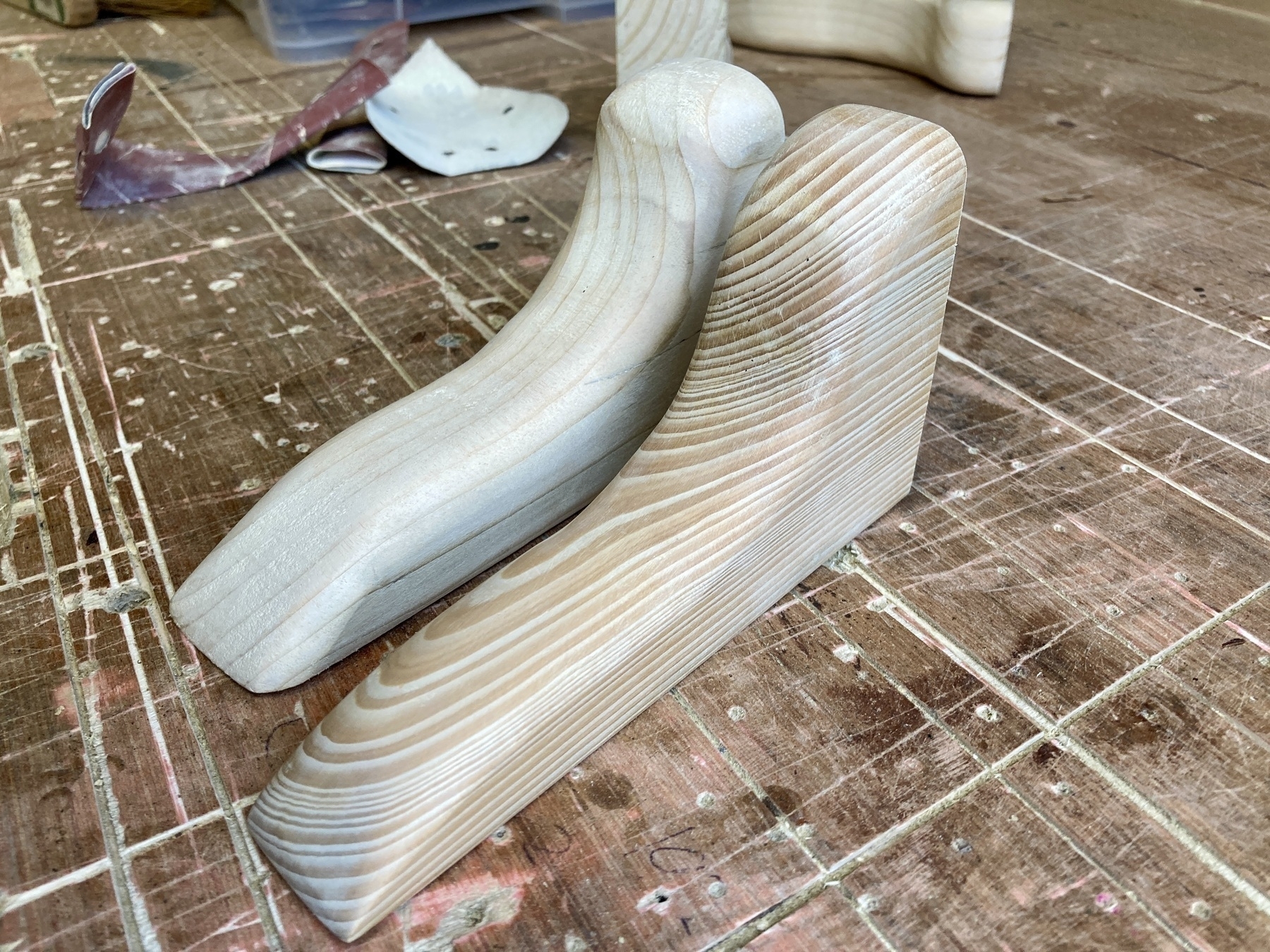 Two carved shelf supports, the one in the foreground made from a darker, harder wood with more grain.