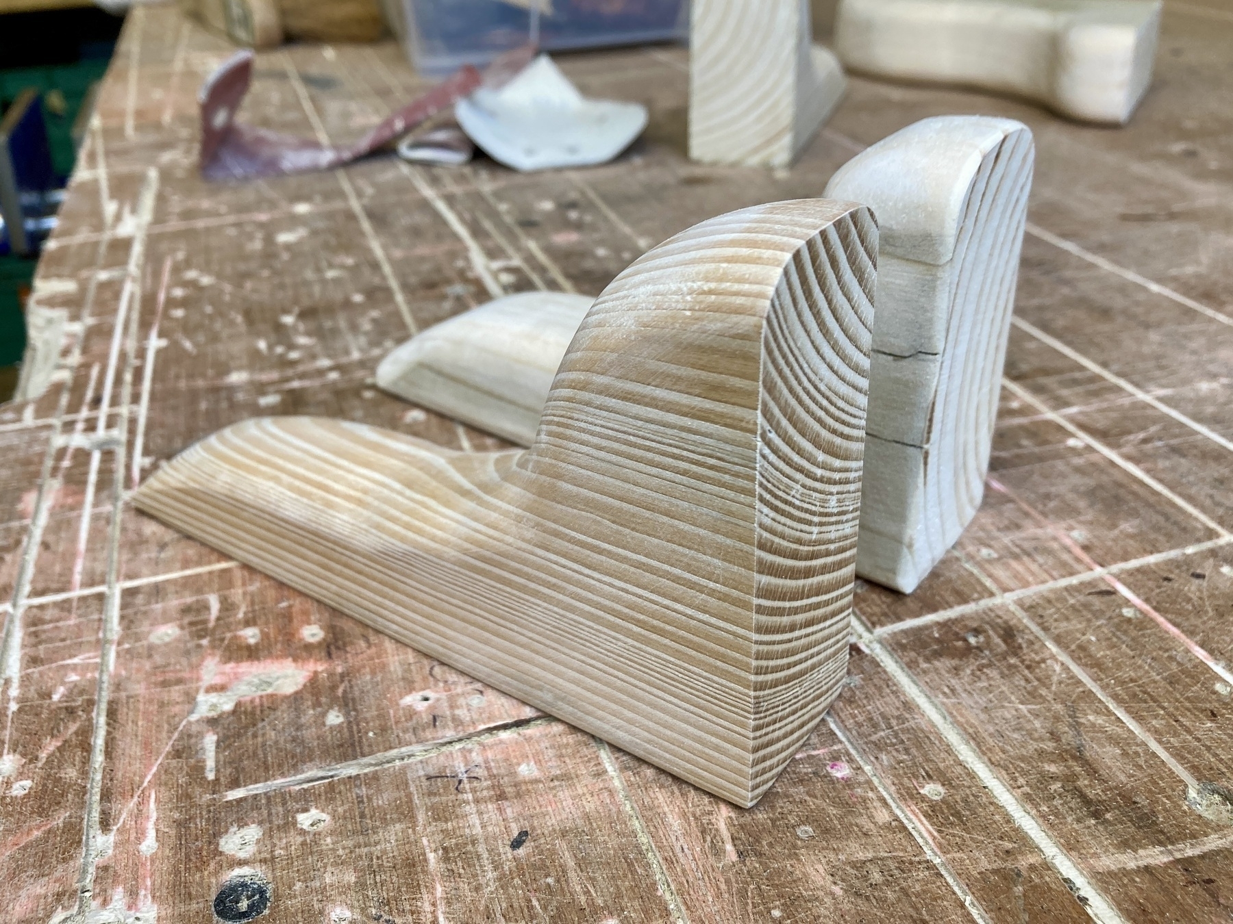 Two carved shelf supports, the one in the foreground made from a darker, harder wood with more grain.