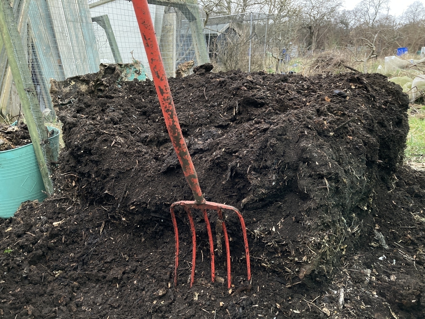 A pile of mature compost with a red pitchfork in front. 