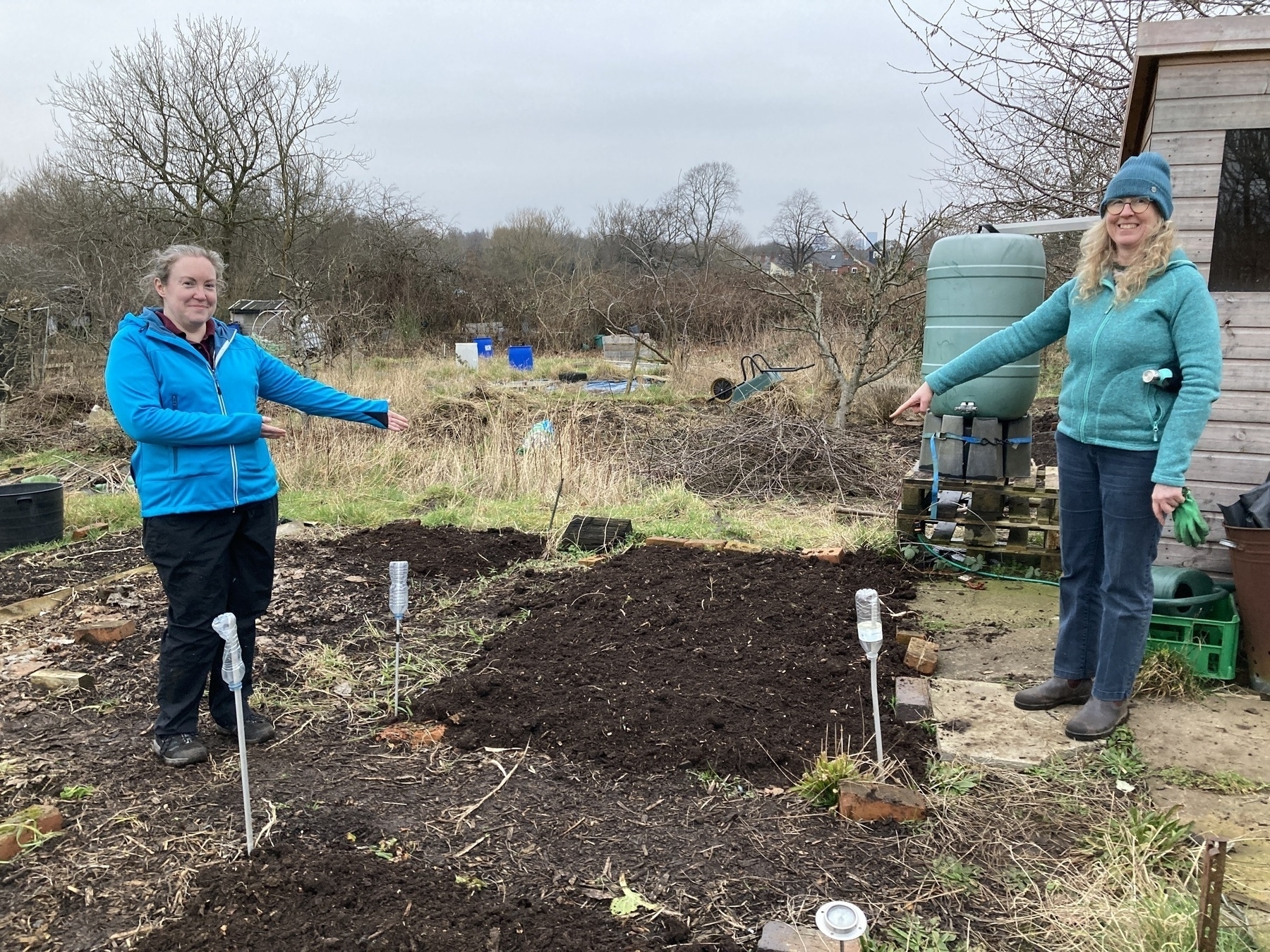 Two women (l-r Laura, Fiona) pointing at a vegetable plot which has been freshly covered in compost.