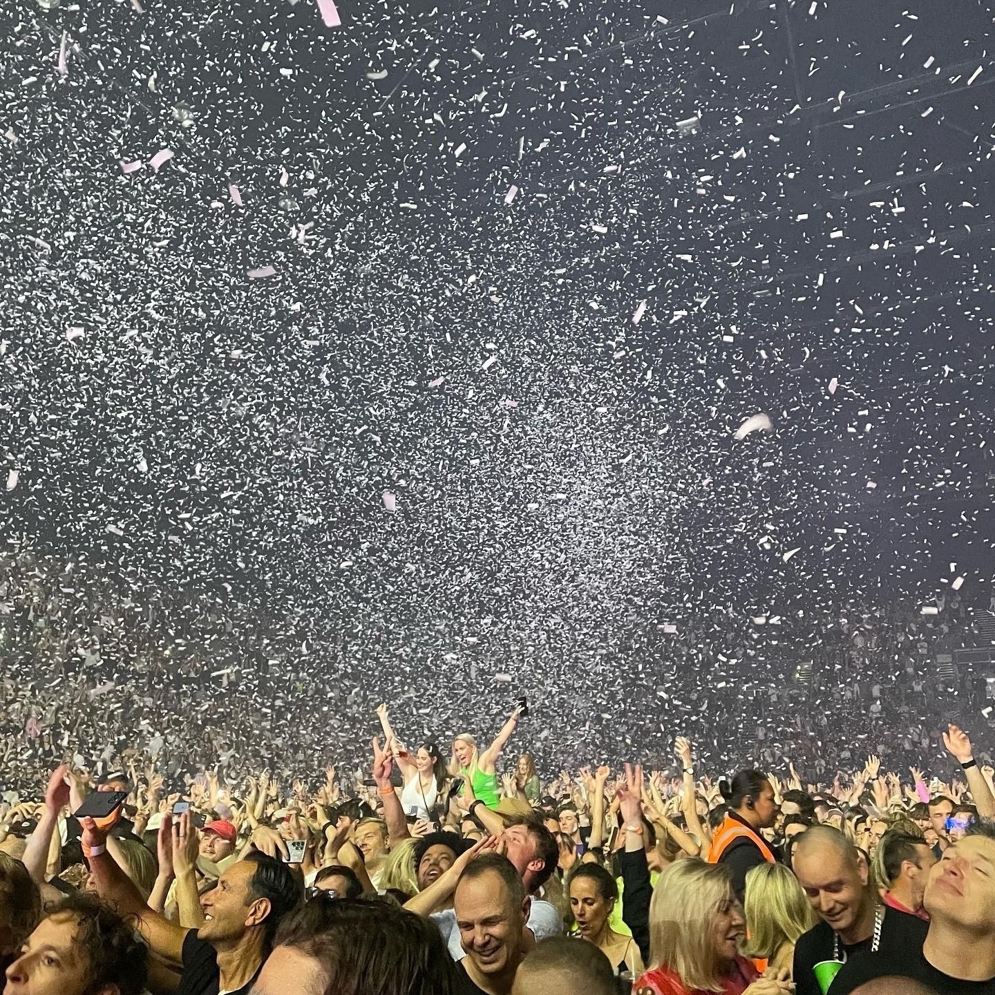 A concert crowd seemingly stretching to the horizon, under a blizzard of white paper confetti 