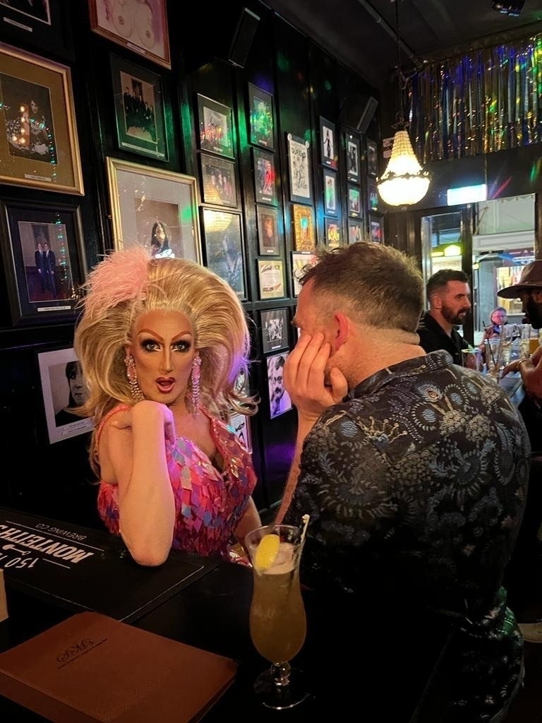 A man looks directly at a drag queen who looks directly at us. A study in obsession. 