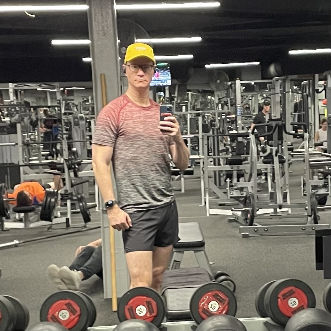 Early morning gym photo in a mirror with a weight rack in the foreground 