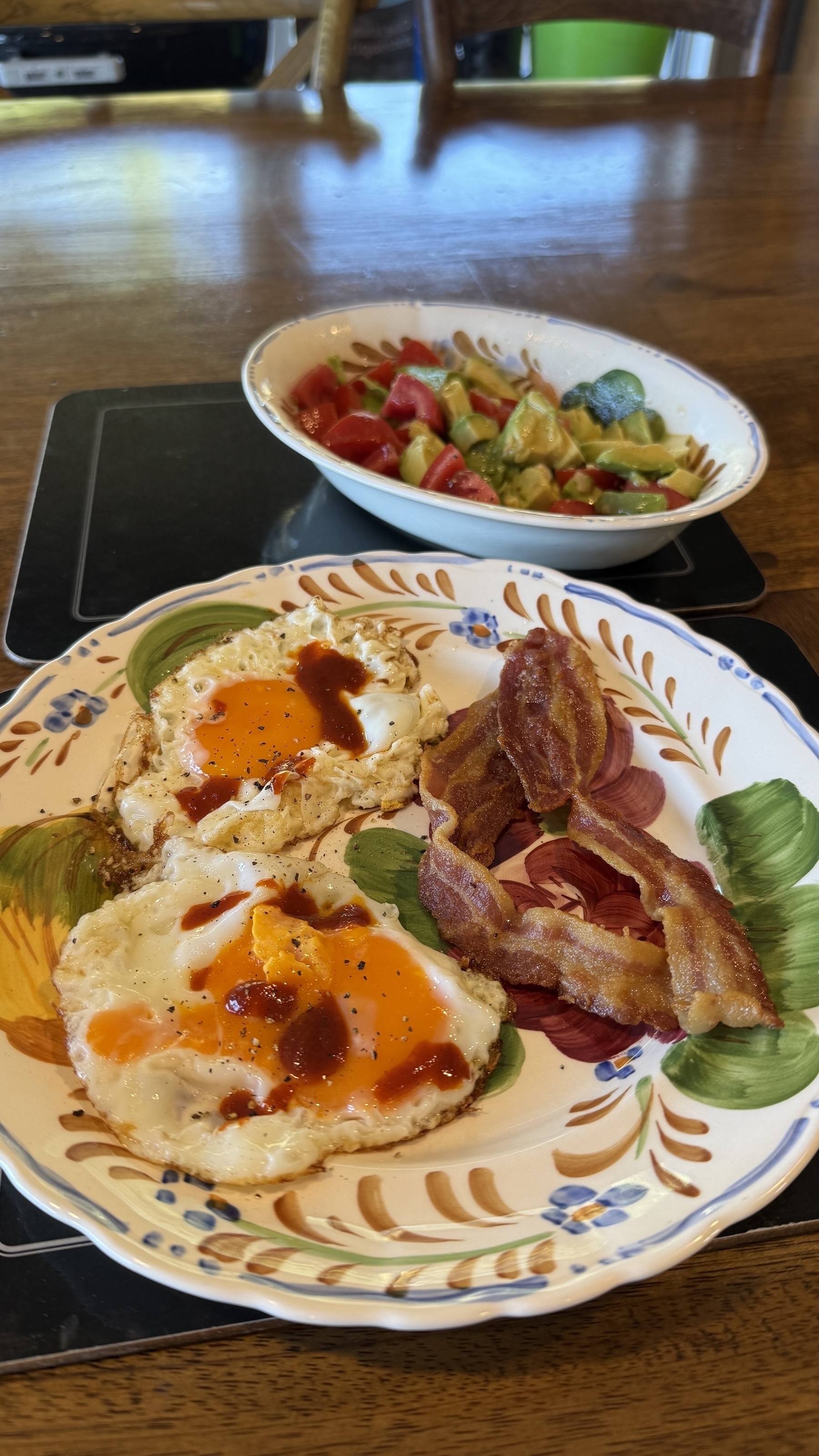 Fried eggs, hot sauce, bacon, and tomato and avocado salad 