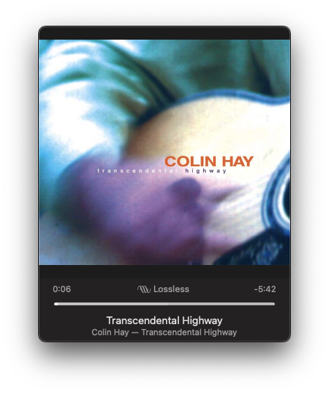 A blurred image shows a close-up of a person playing guitar, with the album Transcendental Highway by Colin Hay displayed.