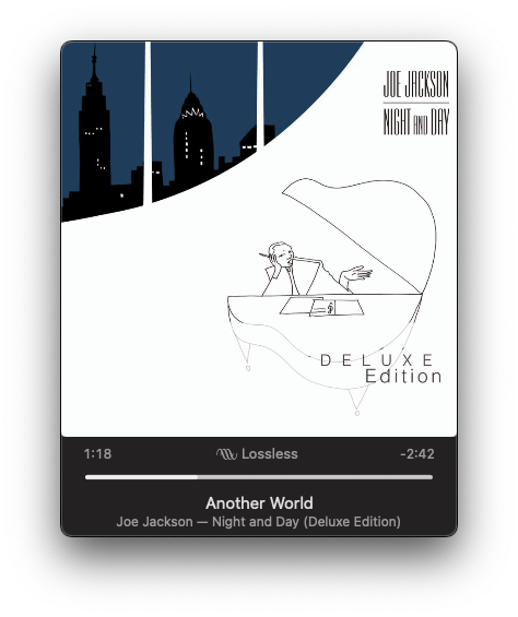 The image features an album cover with a skyline silhouette and a line-drawn figure of a person lying on a piano, titled Joe Jackson Night and Day (Deluxe Edition), alongside a music player showing the song Another World.