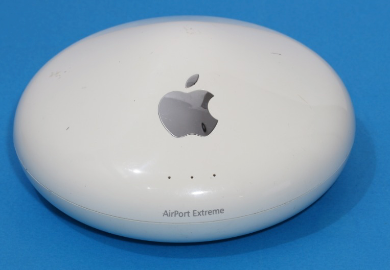 Auto-generated description: A white, oval-shaped Apple AirPort Extreme wireless router with the Apple logo on top is placed against a blue background.