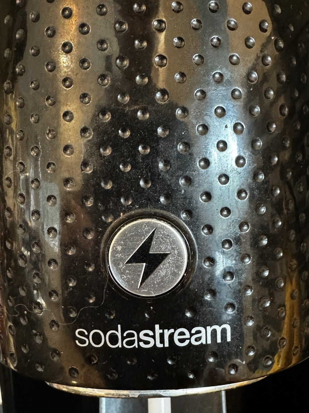 A textured black surface with small round indentations, featuring a circular symbol with a lightning bolt and the text "sodastream" below it.