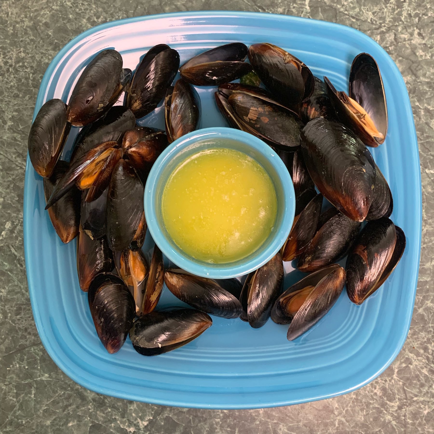 Freshly cooked mussels on a plate surrounding a bowl of melted butter