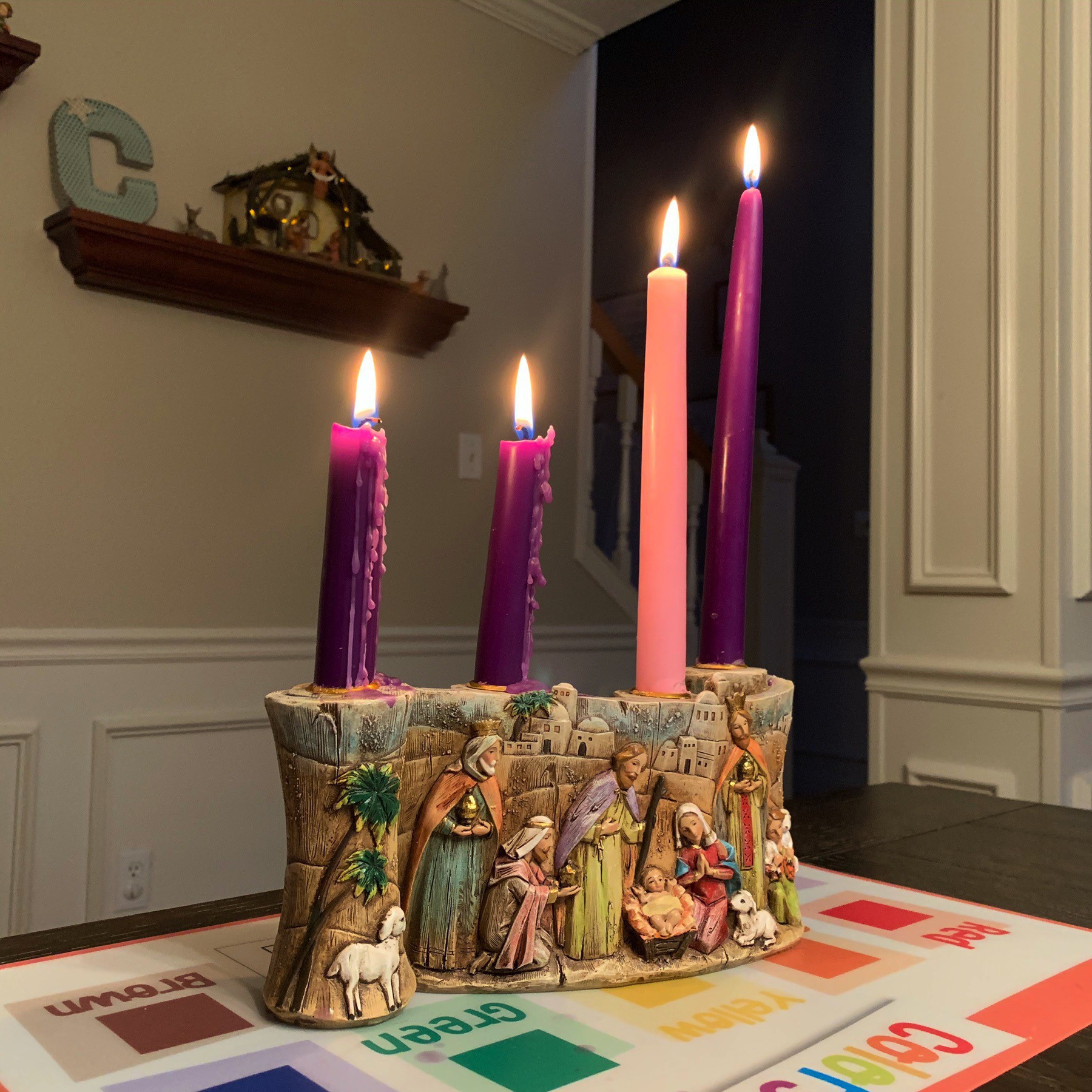 Four Advent candles lit with nativity scene in the background.