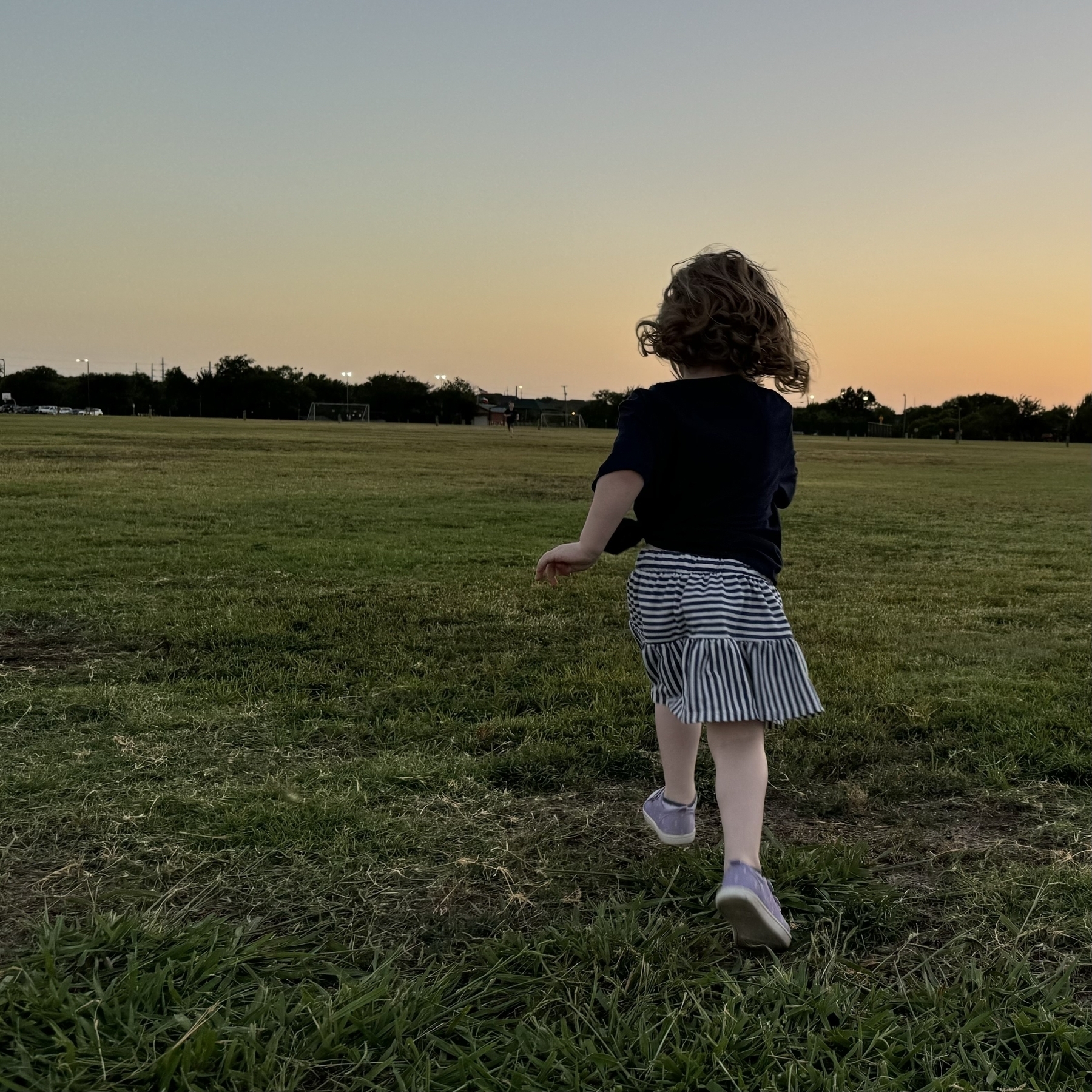 Girl runs across open field at sunset