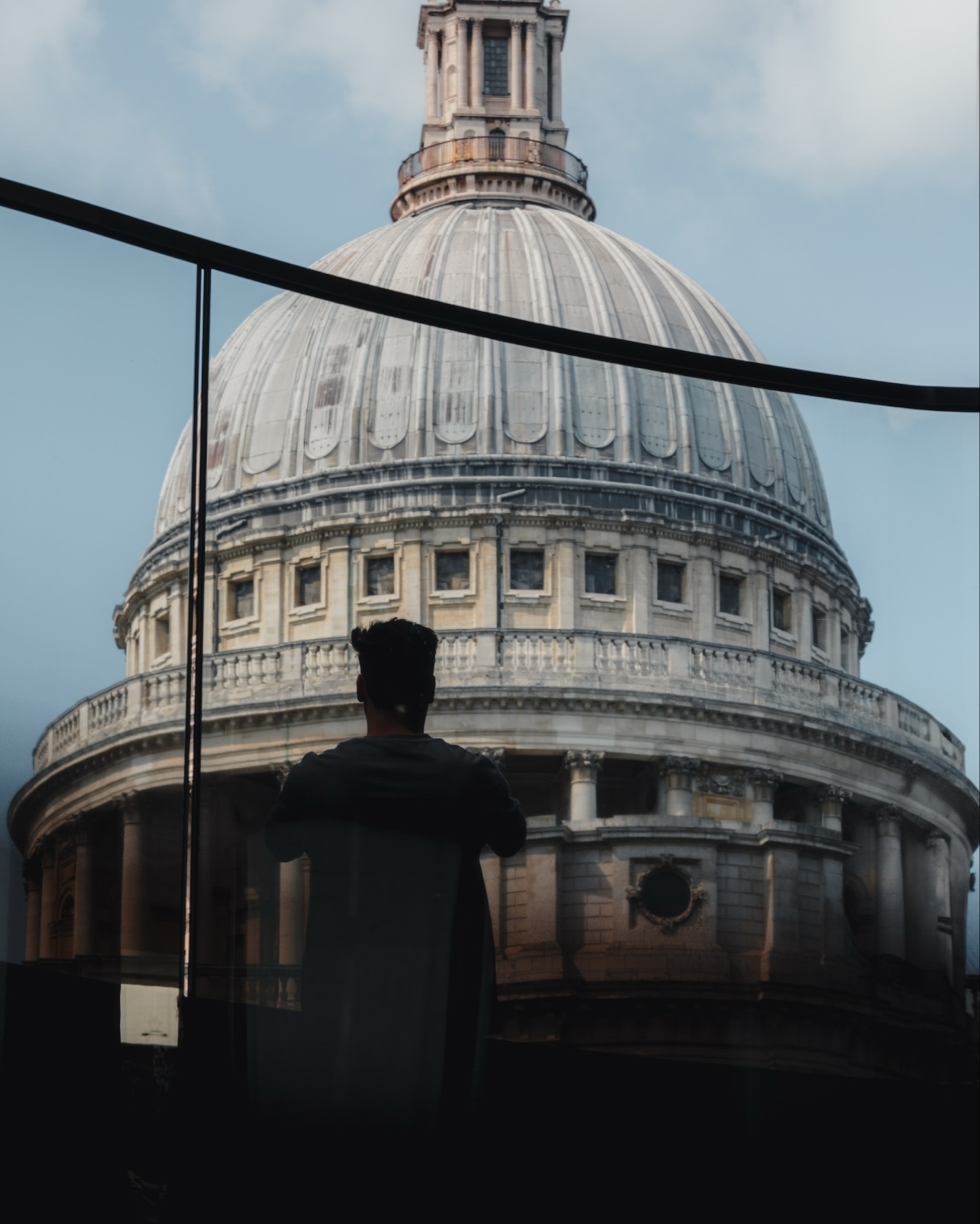 A person looking at the dome of St. Paul's Cathedral through a glass window, capturing the historic architecture under a clear sky.