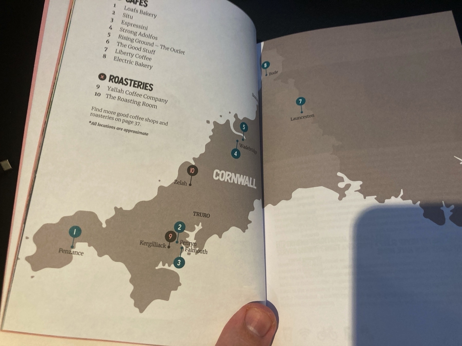 A book opened on a map that spreads across both pages; on the pages are pinned locations with numbers and their names attached. There is a list with the corresponding numbers and associated names of independent coffee shops and roasteries.