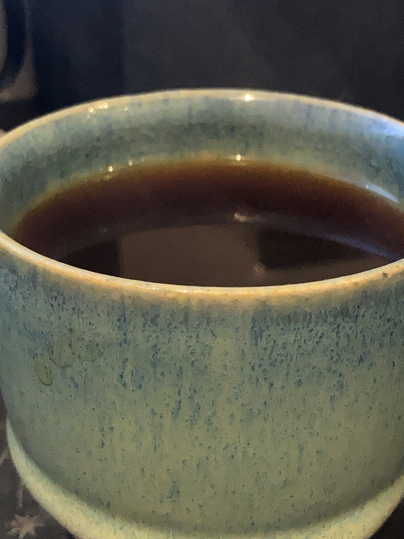 A cup of coffee close-up, with steam escaping from the cup. The cup is ceramic, decorated in a variety of ocean-inspired blues, and made locally!
