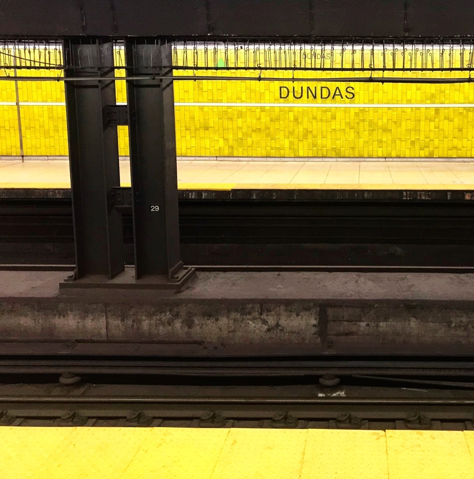 Auto-generated description: A subway platform with yellow tiles has a sign that reads DUNDAS.