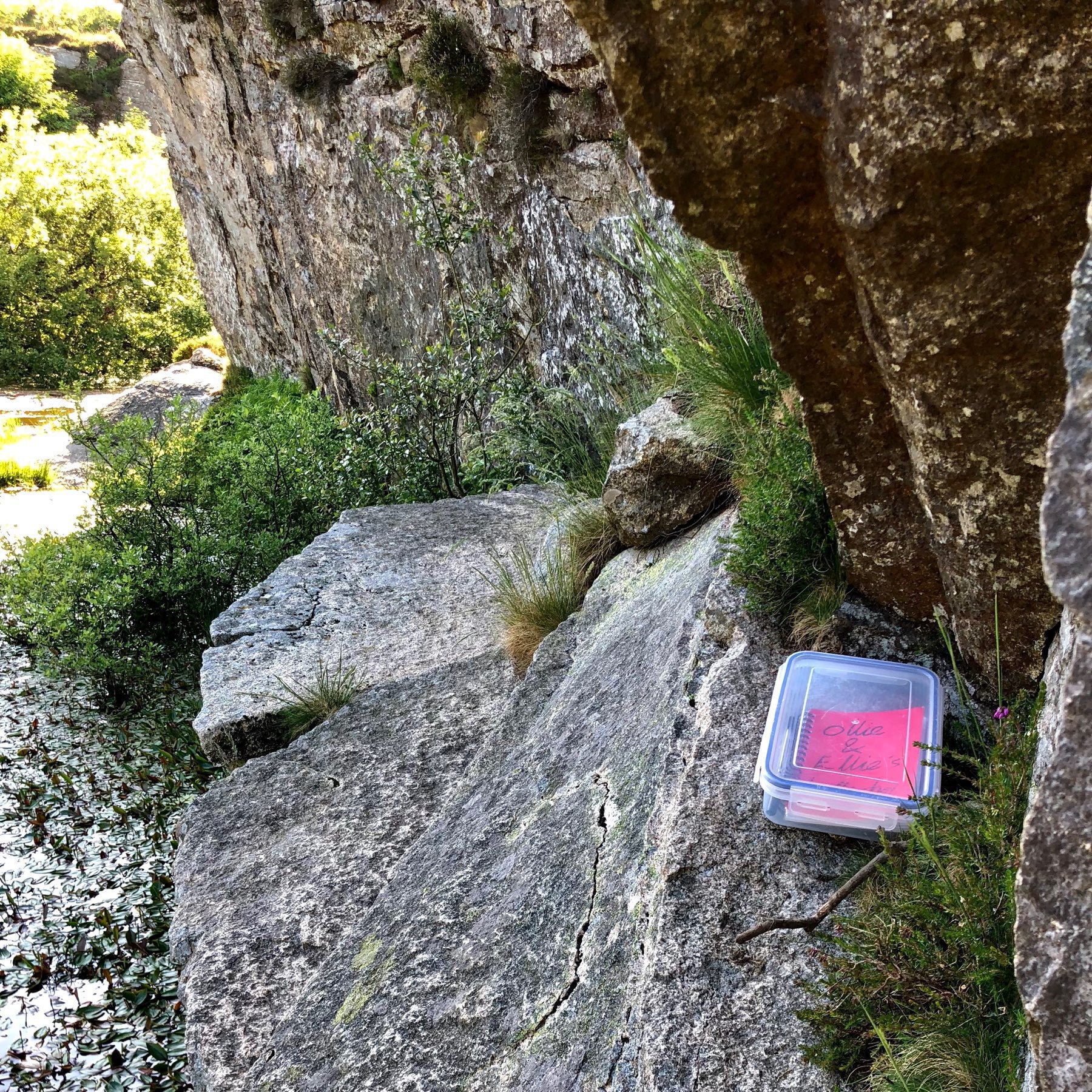 A letterbox for people to leave notes in, perched on a rock wall by a lake