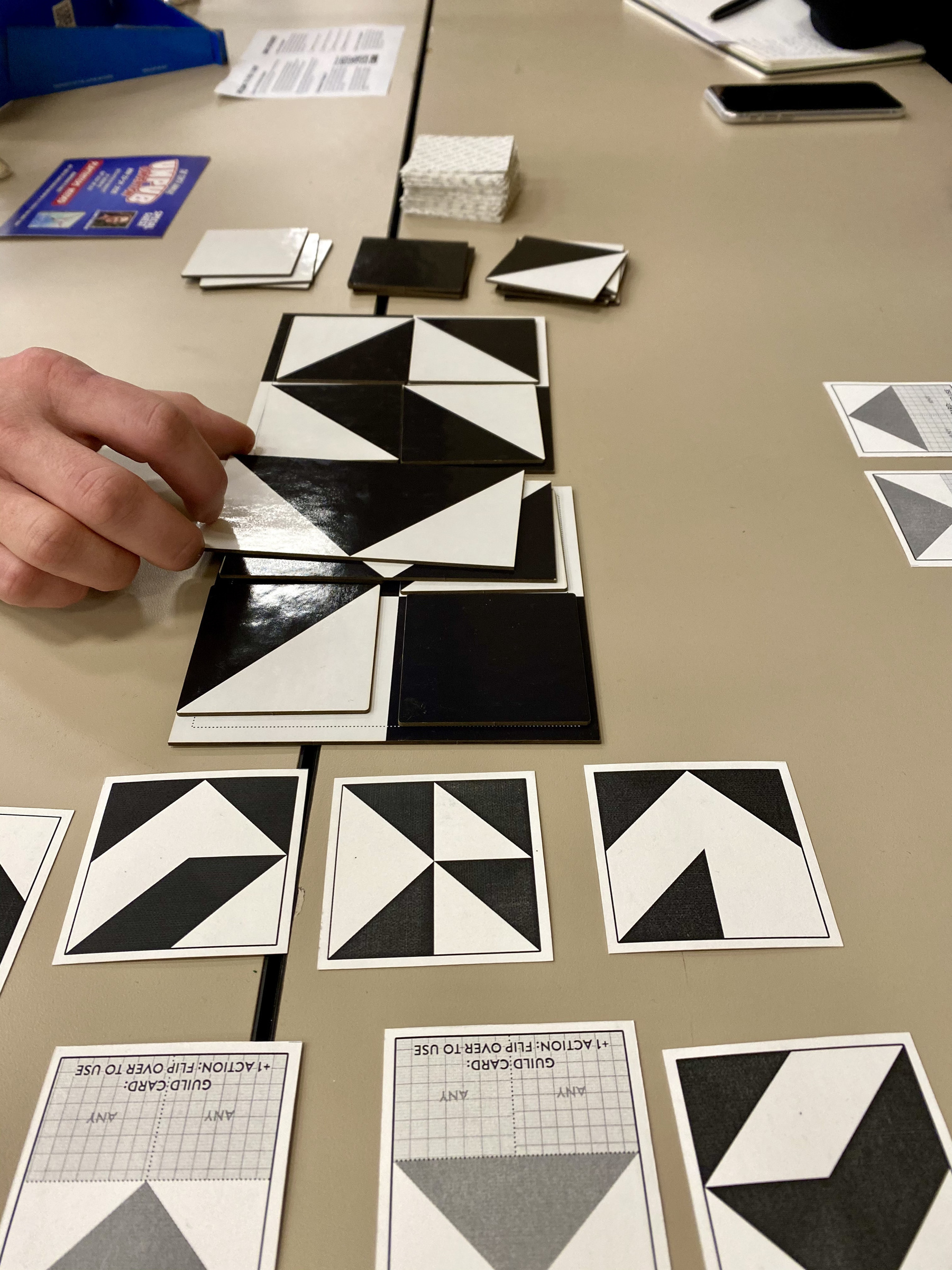 Board game with black and white tiles being played on a table with a person's hand rotating one of the tiles