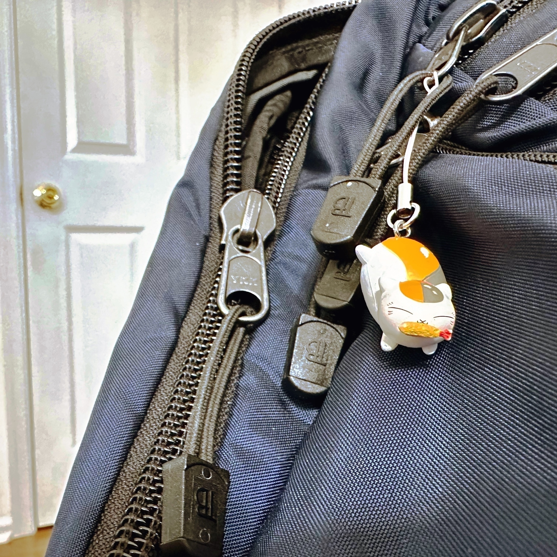 Closeup of backpack with charm of cartoon cat eating sushi attached
