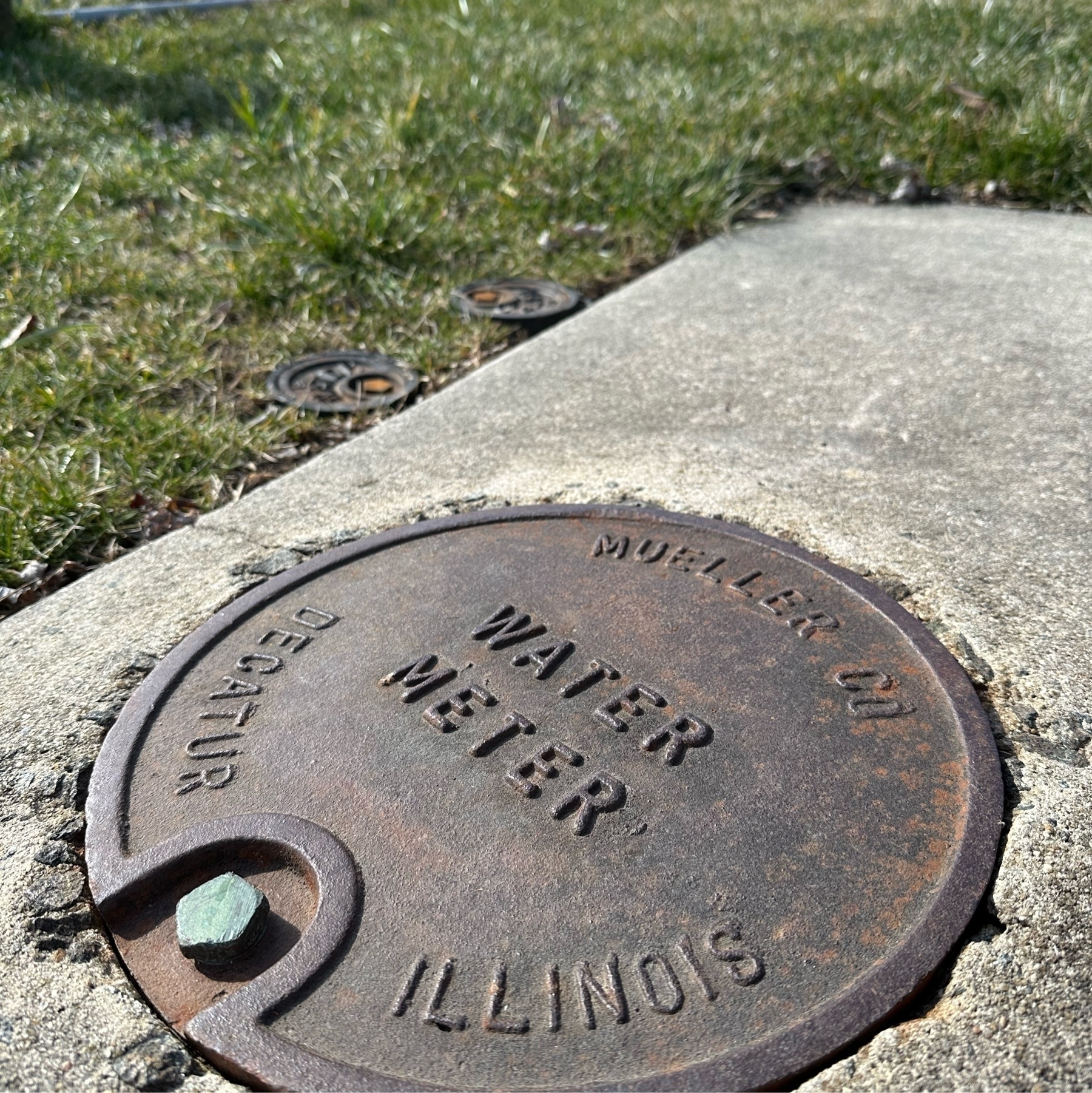Photo of a metal water meter cover in cement, with the text "Water Meter" and "Decatur Illinois" visible.