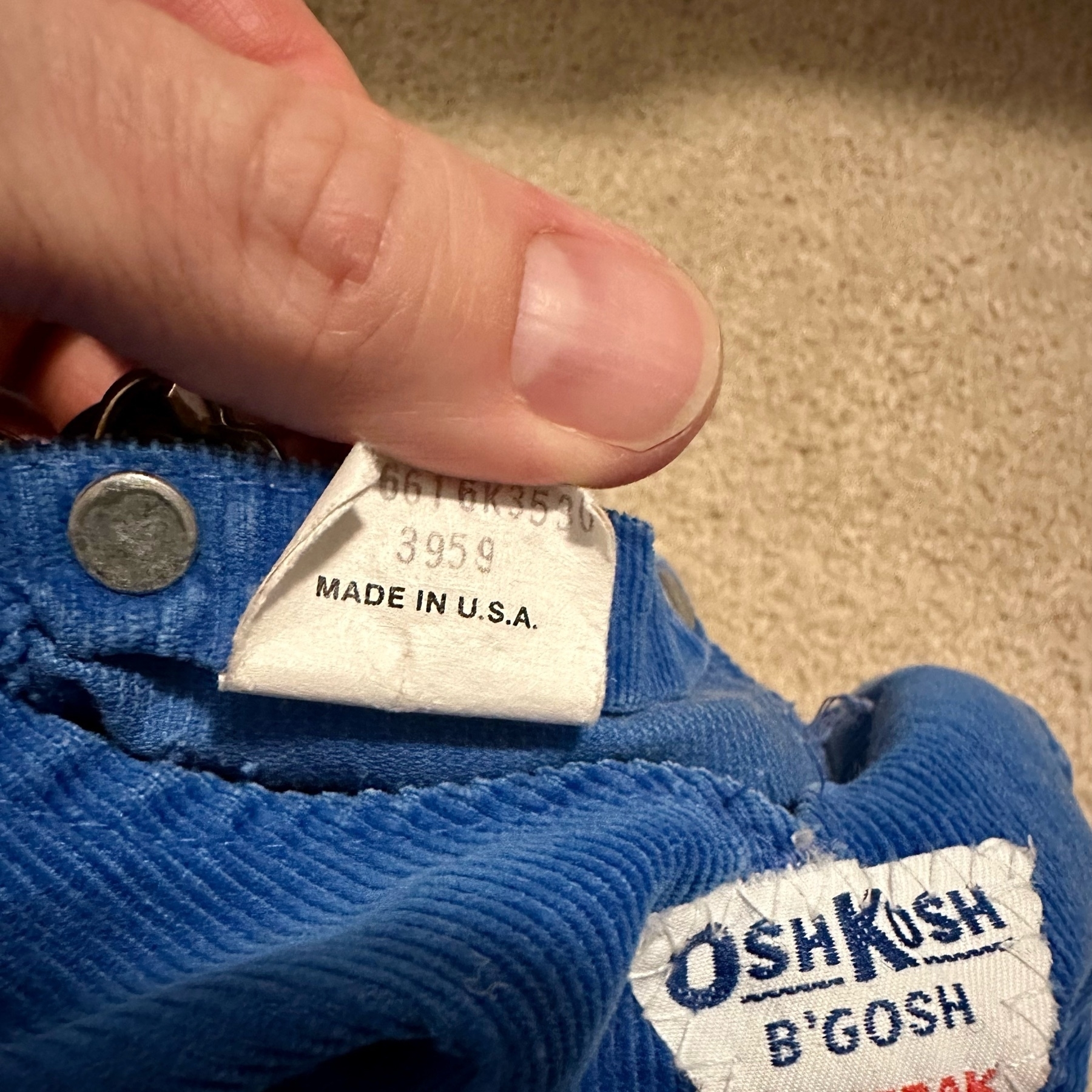 A pair of OshKosh B'gosh baby's overalls, closeup on the label, which says "Made in U.S.A."