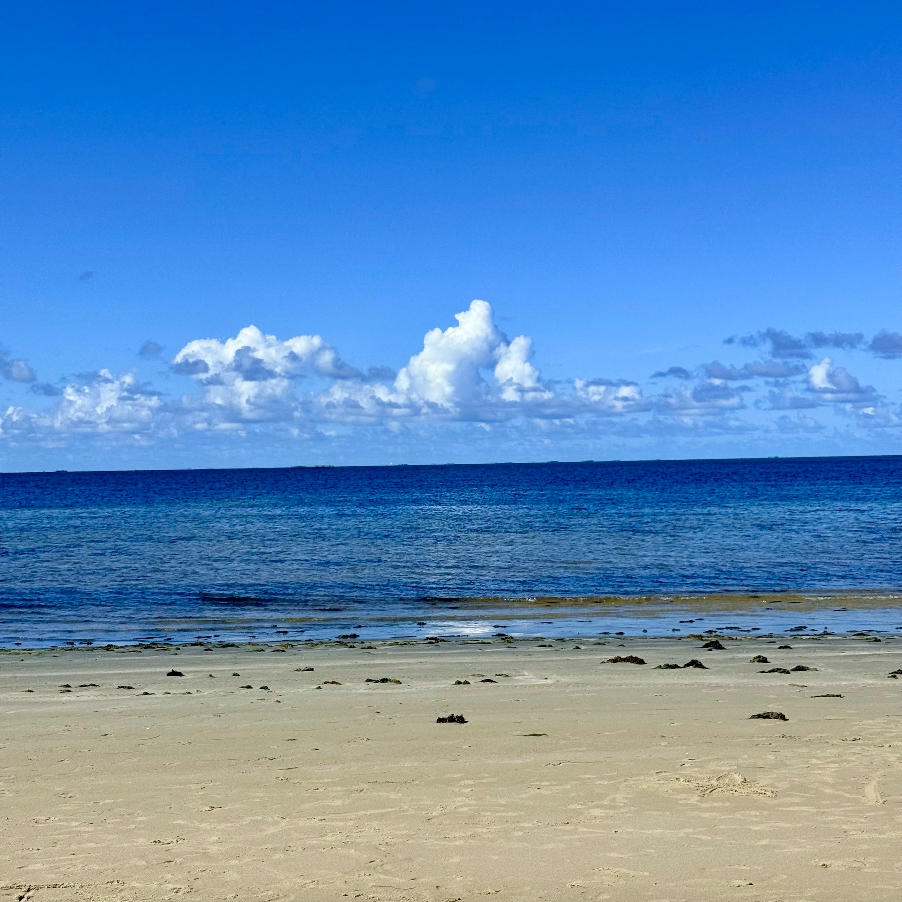 Uma praia tranquila com areia clara e um mar azul sob um céu parcialmente nublado.