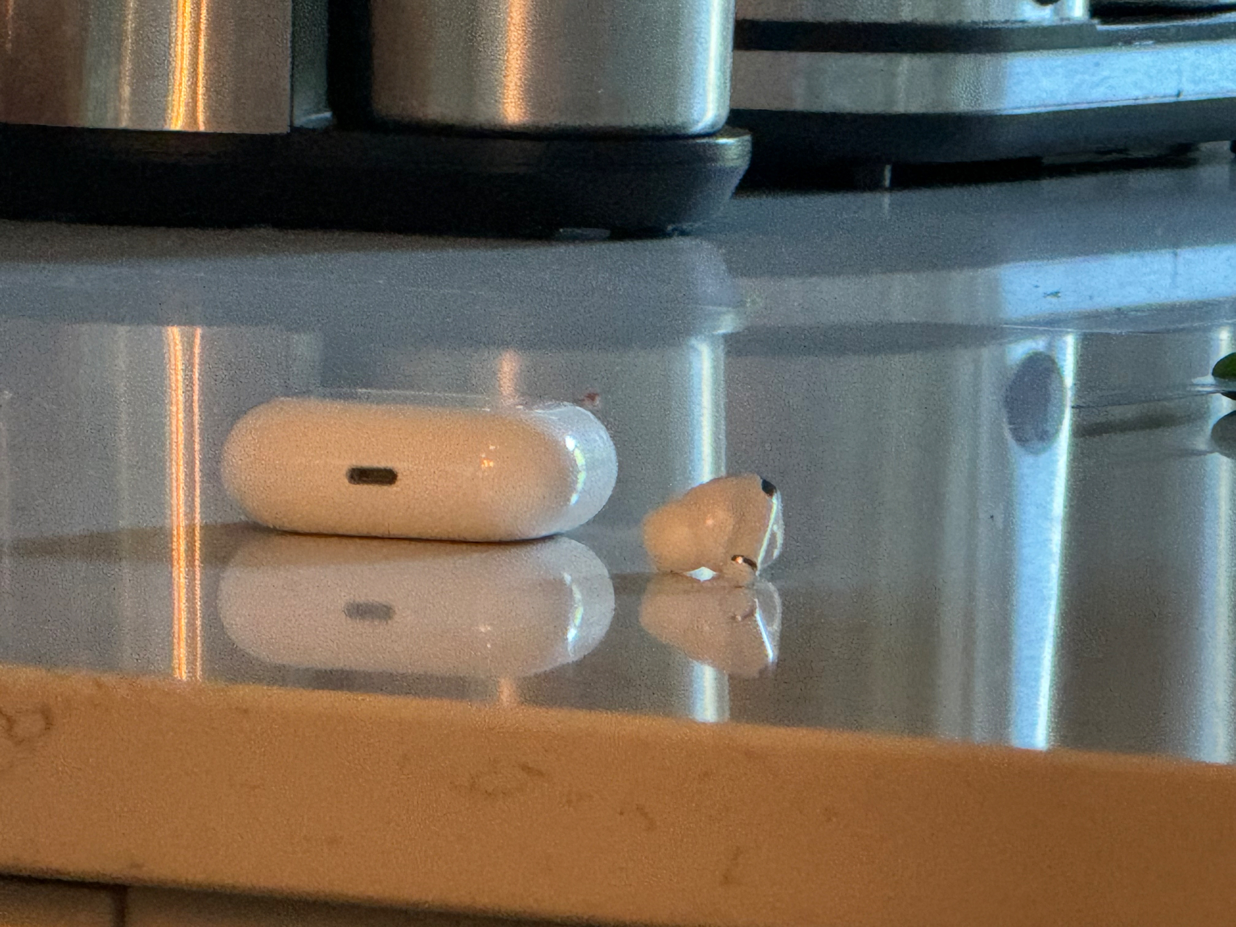 A single air pod sitting loose on a kitchen counter right next to its case 