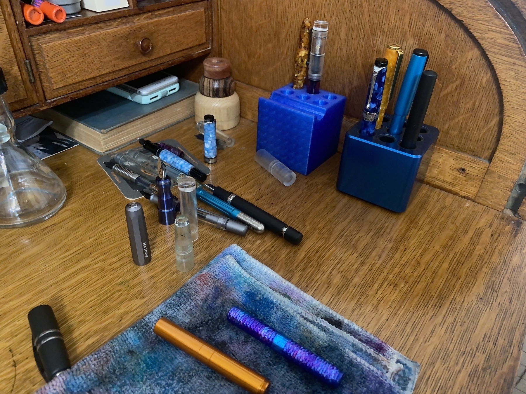Various fountain pens laying on a desk in pieces after cleaning, with additional pens in two pen stands.
