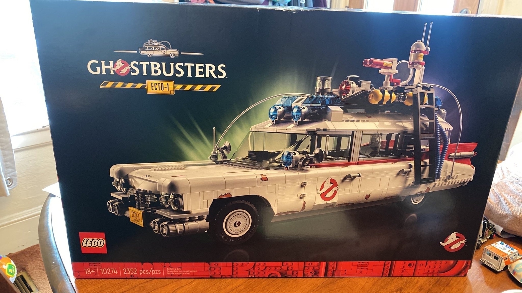 The Ghostbusters Ecto 1 Lego set sitting on a table with a couple Matchbox cars next to the box.