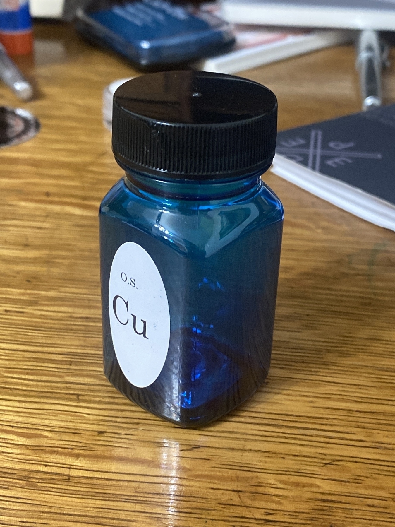 An empty bottle of fountain pen ink, with blue/turquoise ink clinging to the walls of a bottle. The bottle is sitting on a vintage oak desktop.