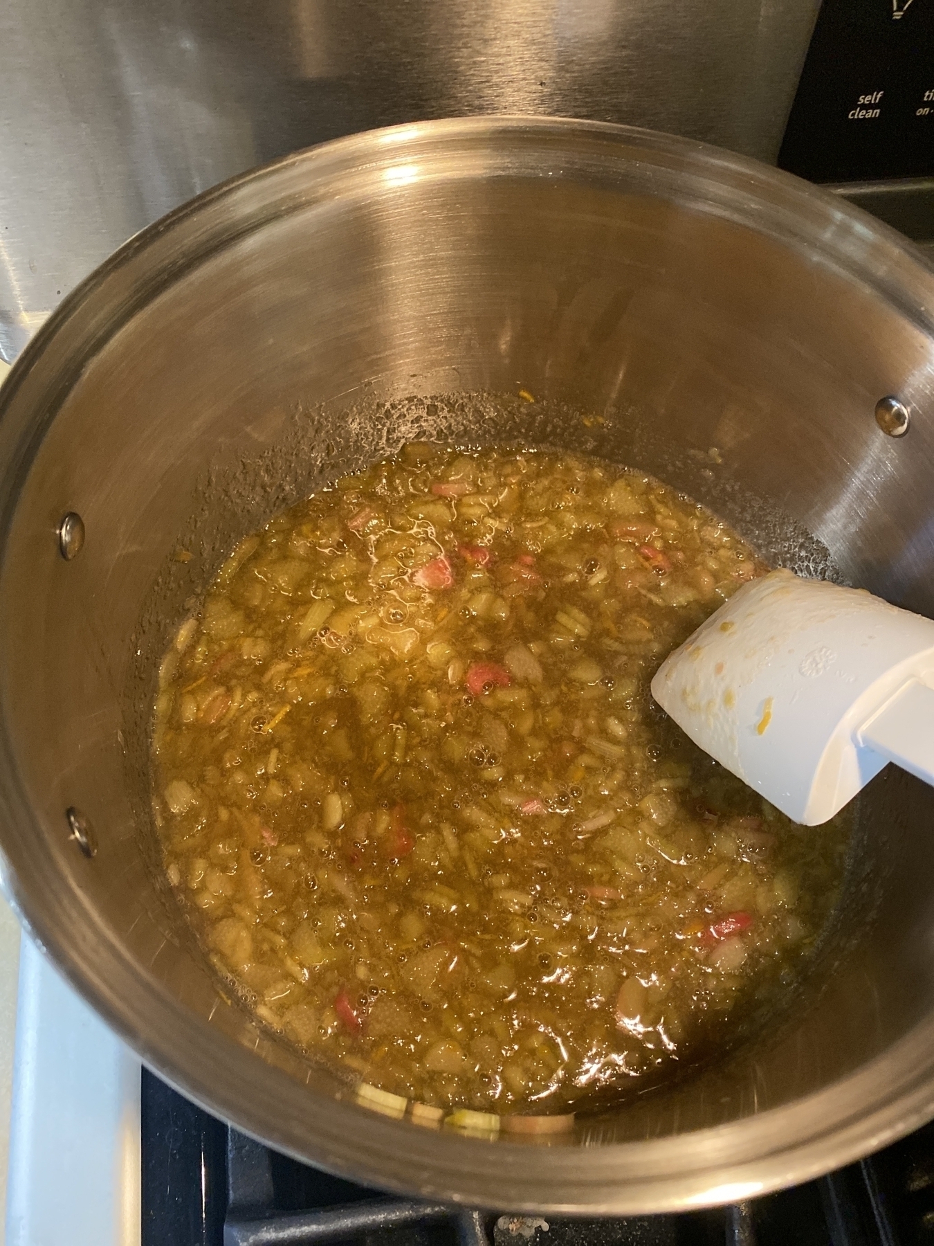 A large pot on a stove filled with the makings of rhubarb orange jam, and a white spatula. 