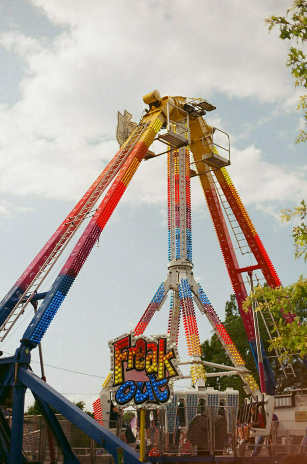 A dynamic image of a thrill ride called 'Freak Out' at its peak motion, with seats filled with riders flung into the air. The ride is brightly colored with yellow, red, blue, and green, and the name of the ride is prominently displayed in a stylized font with lights.