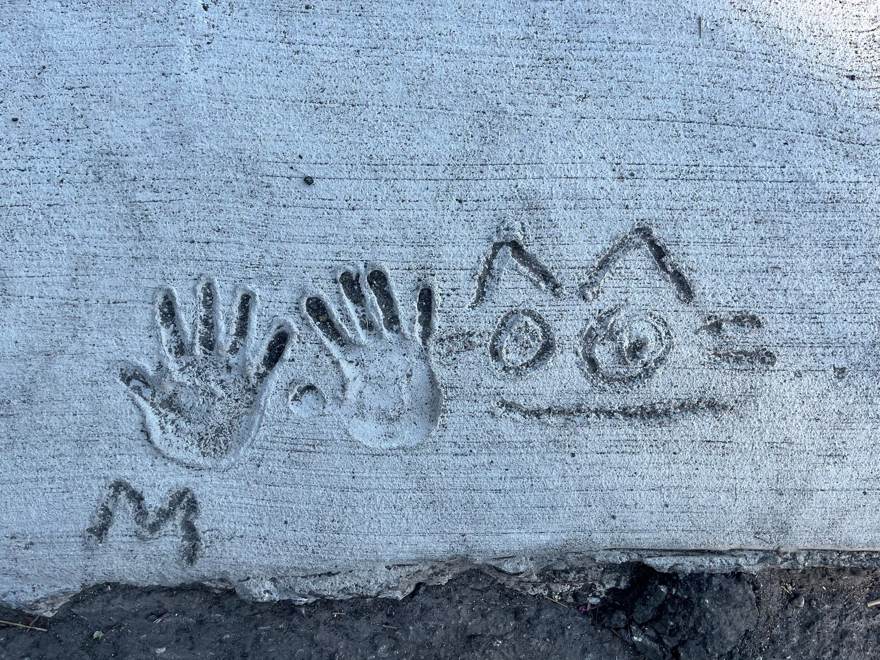 Two handprints and a cat drawing are imprinted in concrete.&10;