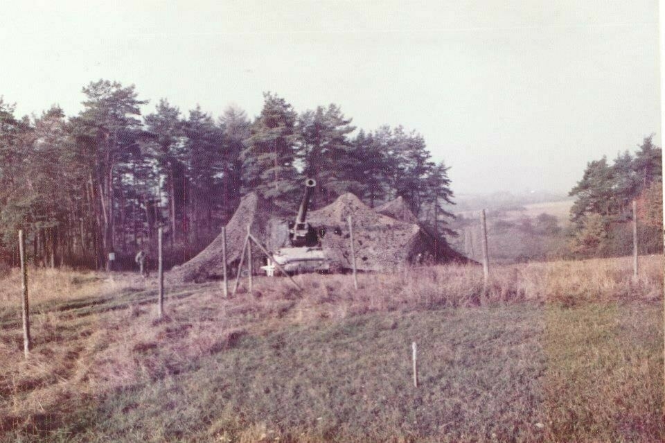 Photo of an 8-inch howitzer under a camouflage net taken in Germany, probably in Grafenwöhr in the fall of 1983