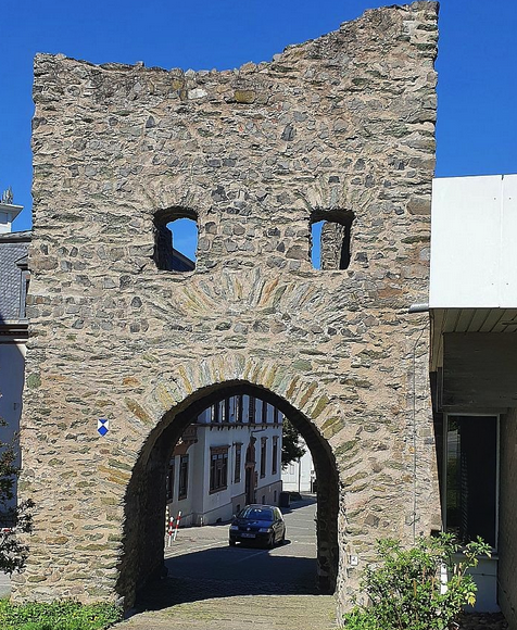 medieval city gate made of stone with a big mouth, which a car is about to drive through, and two eyes