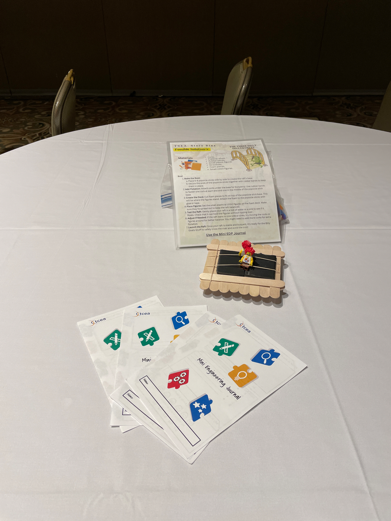 Auto-generated description: A round table is set with worksheets, a calendar on a small stand, and an informational flyer in a plastic cover.