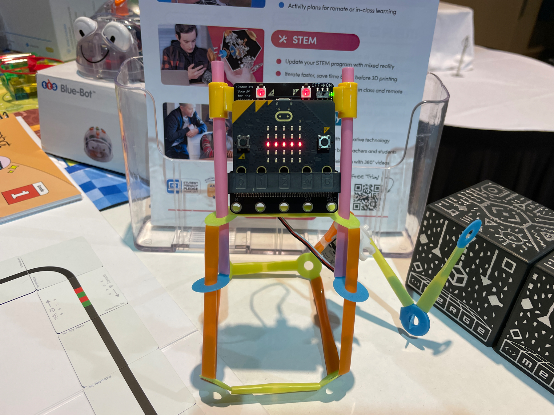 Auto-generated description: A microcontroller is displayed on a colorful, makeshift stand made of straw-like materials, surrounded by educational tools and literature.