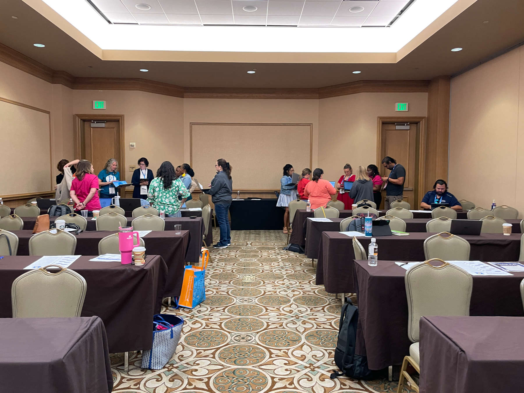 Auto-generated description: A group of people are gathered around tables in a conference room, seemingly engaged in discussions or activities, with some individuals standing and others sitting.